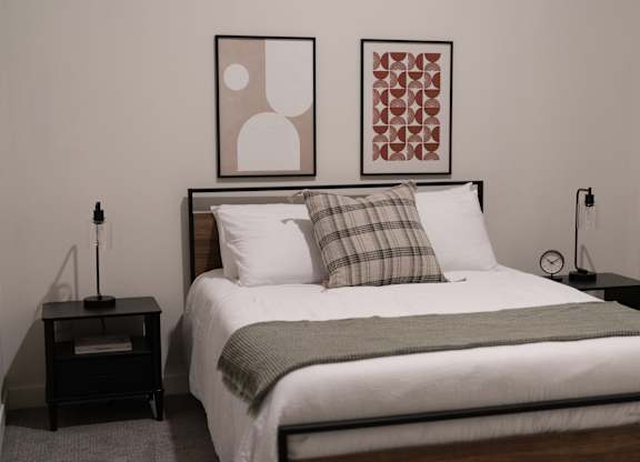 A bed with a white comforter and a green throw is flanked by two nightstands with lamps.