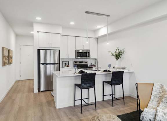 A modern kitchen with a white island and black chairs.