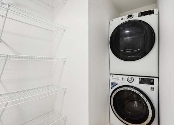A white dryer is stacked on top of an empty dryer in a white laundry room.