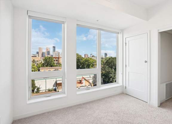 A room with three windows showing a cityscape and greenery outside.