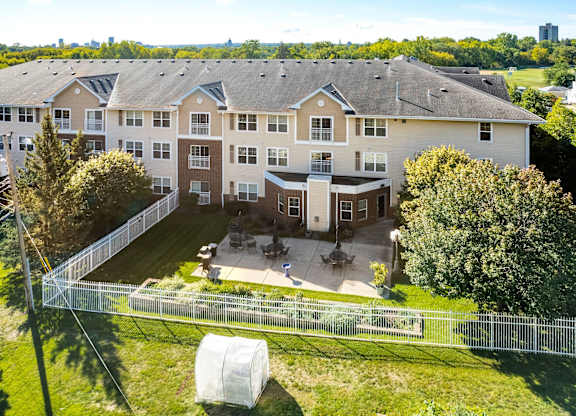 A large apartment complex with a fenced in yard and a tree.