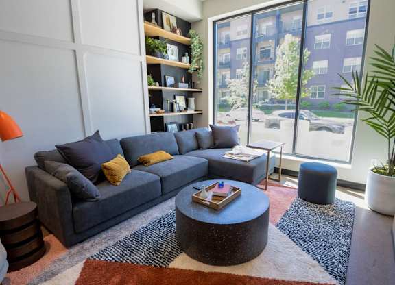A living room with a grey couch, a round coffee table, and a large window.