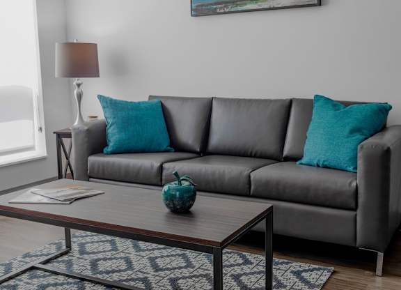 A grey couch with a blue pillow and a blue vase on a coffee table.