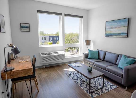A living room with a brown couch, a wooden desk, and a painting on the wall.