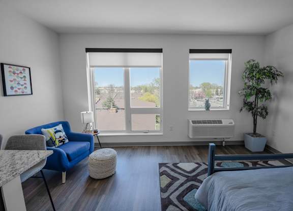 A bedroom with a blue couch and a large window with a view of trees and a building outside.