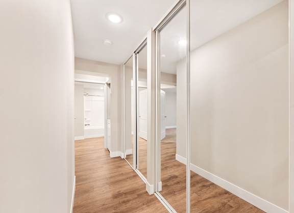 A hallway with a mirrored wall and wooden floors.