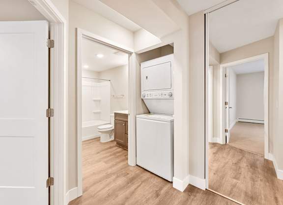 A white door is open to a bathroom with a toilet, sink, and a white fridge.