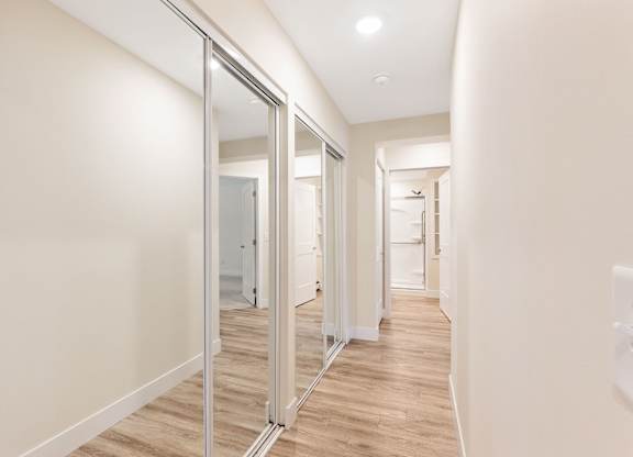 A hallway with a white wall and a wooden floor.