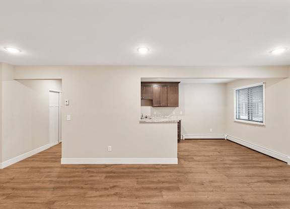 A large empty room with wooden floors and a kitchenette.