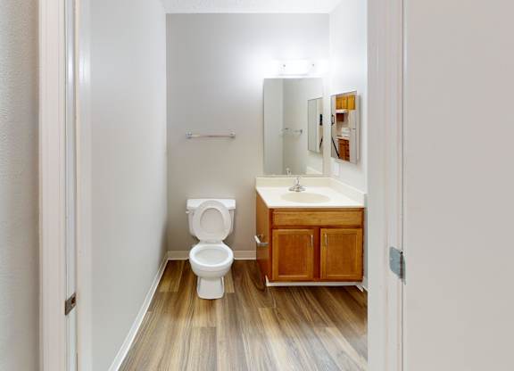 A white bathroom with wood flooring and a wooden cabinet.