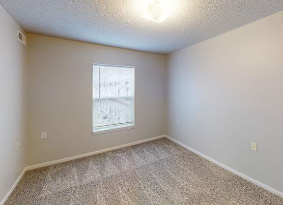A room with a window and a carpeted floor.