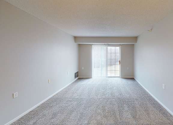 A large, empty room with a carpeted floor and a window with blinds.
