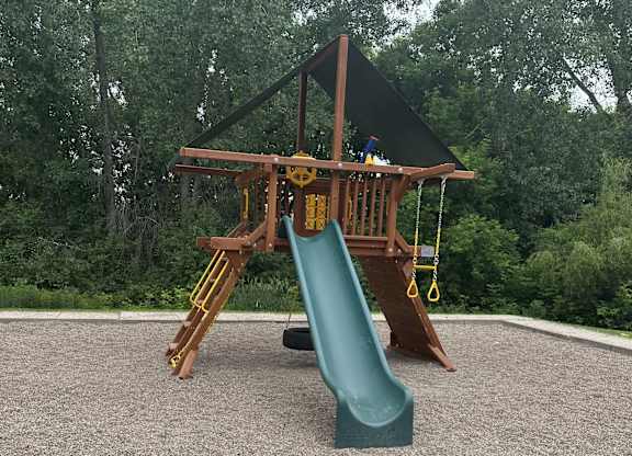 A playground with a green slide and a brown wooden structure.
