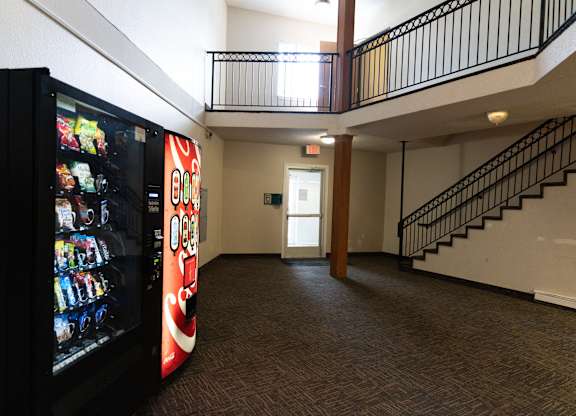 A vending machine is on the left of a hallway with a staircase on the right.