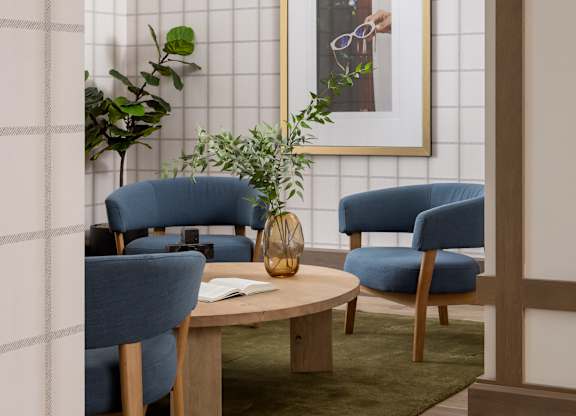 A living room with a blue chair, a wooden table, and a framed picture on the wall.