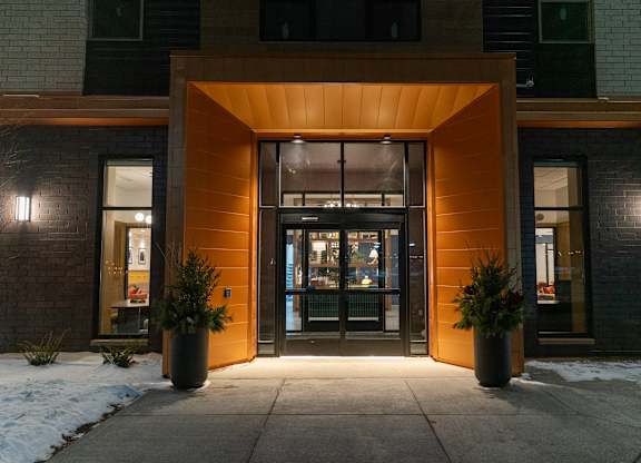 The entrance to a building with a glass door and two potted plants on either side.