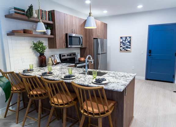 A kitchen with a granite countertop and wooden chairs.