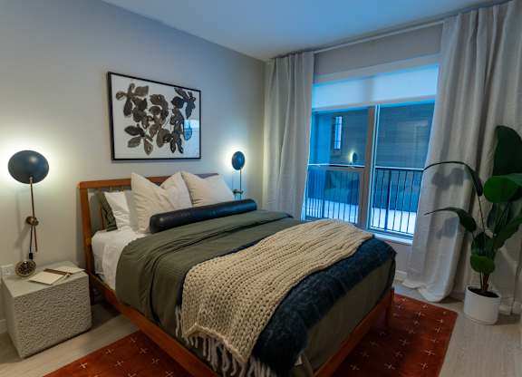 A bedroom with a bed, nightstand, and a plant.