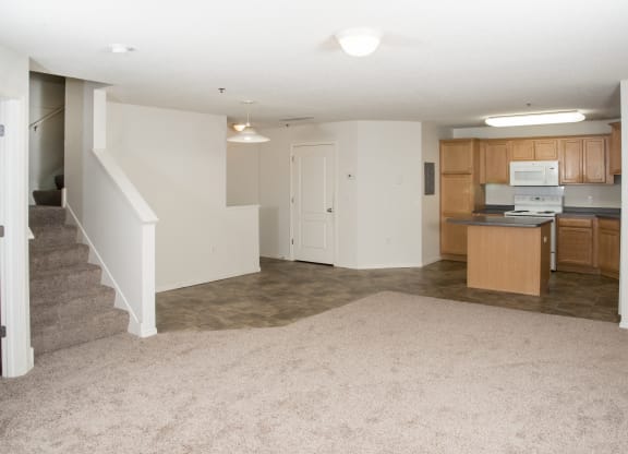 an empty living room and kitchen with a stairway to a room with wood cabinets
