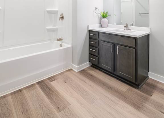 A bathroom with a white tub, sink, and wooden floors.