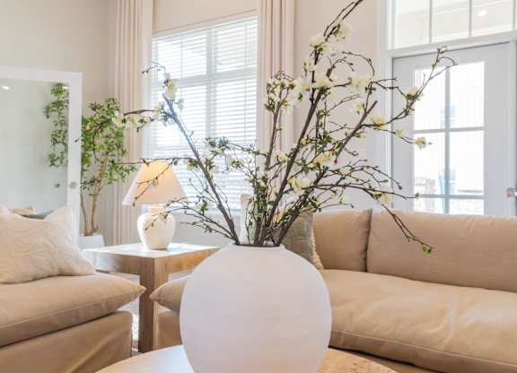 A white vase with branches in it sits on a table in a living room.