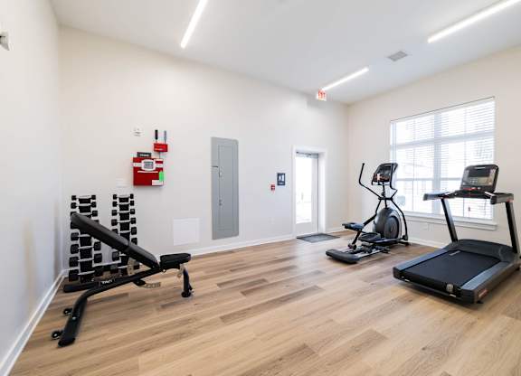 A gym with a treadmill, elliptical trainer and a weight bench.