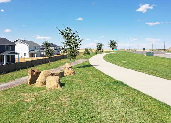 a sidewalk and grassy area with trees and houses in the background