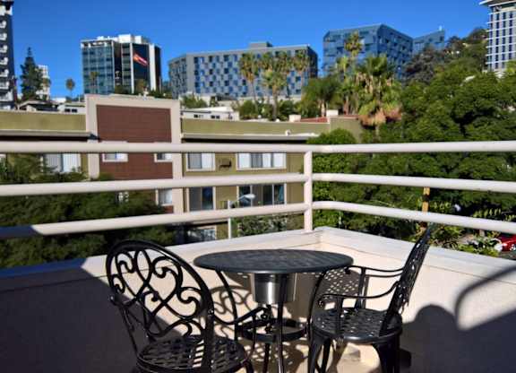 A balcony with a table and chairs overlooking a cityscape.