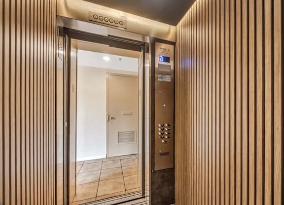A modern elevator with a wooden panel design and a control panel with buttons and a touch screen.