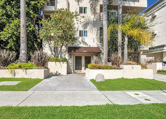 Image of 9025 Alcott Apartment building with a brown awning is surrounded by greenery.