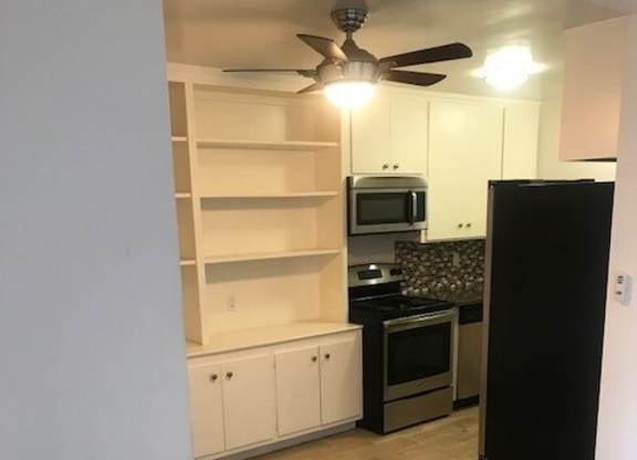 A kitchen with a black refrigerator, wooden floors, and white walls.