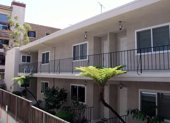 A balcony with a black railing and a tree in front of a building.