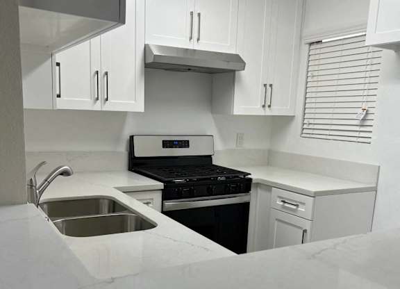 A kitchen with a stove, sink, and cabinets.