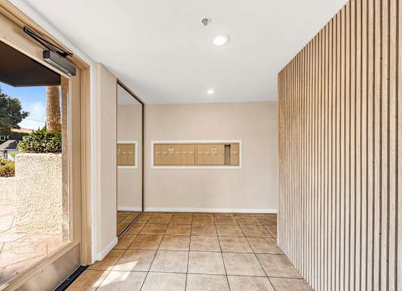 A hallway with a tan wall with mailboxes and a tan tile floor.