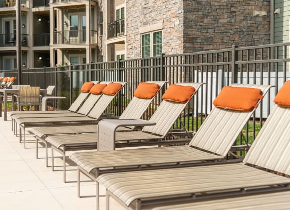 a row of lounge chairs with orange pillows in front of an apartment building at The Whitworth, Williamsburg, 23185
