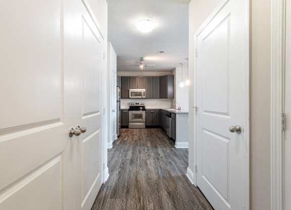 A long hallway with white doors on either side leading to a kitchen.