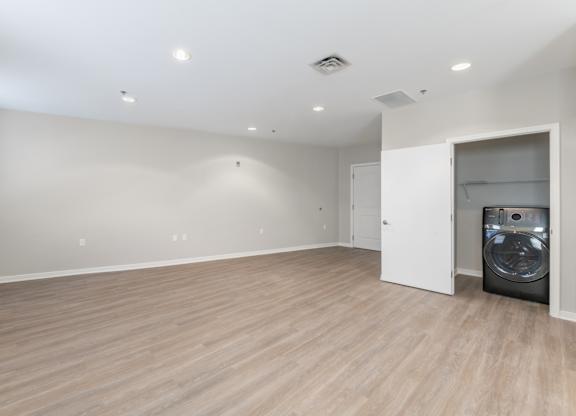 A large empty room with a washing machine in the corner.