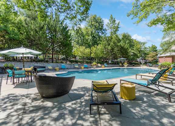 A sunny day at the pool with a green umbrella and blue chairs.