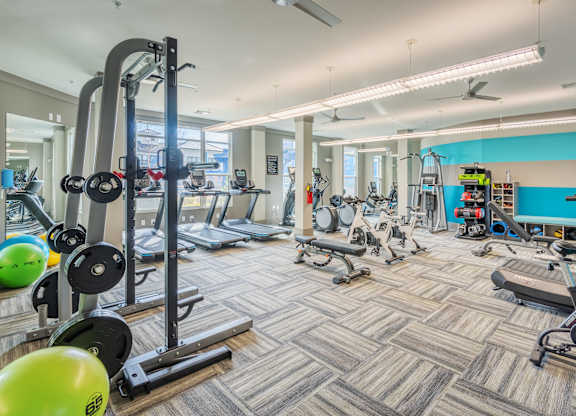 A gym with a variety of equipment including treadmills, weights, and exercise balls.