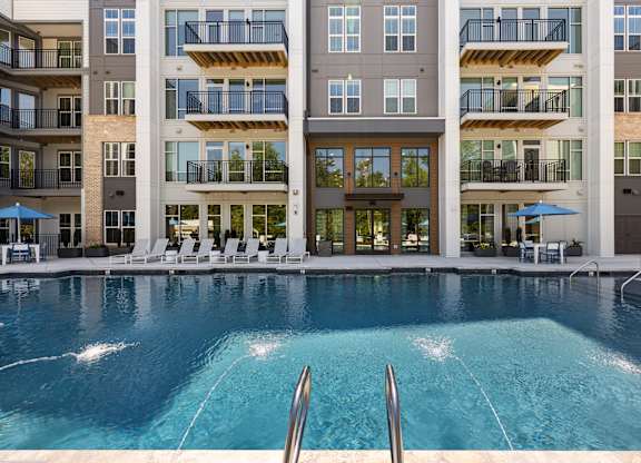 A large swimming pool in front of a multi-story apartment building.