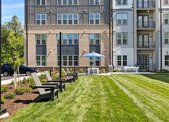 A large grassy area in front of a building with benches and a blue umbrella.
