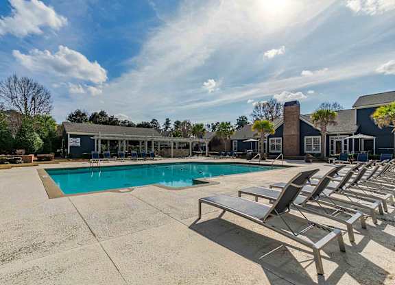 A sunny day at the pool with lounge chairs and a building in the background.