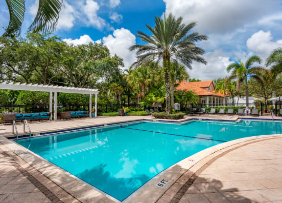 a swimming pool with palm trees and a building in the background at The Villas at Ibis Landing, Parkland, FL