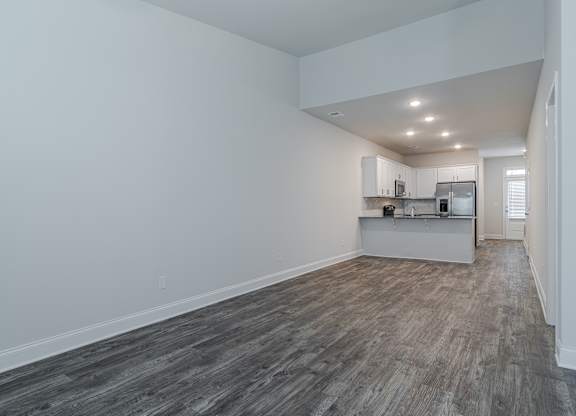 A kitchen with white cabinets and a refrigerator is visible in the background.