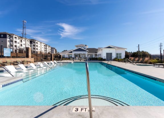 a swimming pool with white chairs and a building in the background at Capstone at Banks Crossing, Commerce