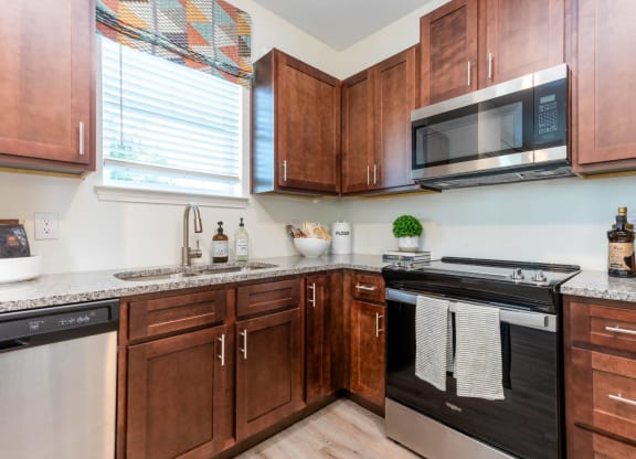 a kitchen with wooden cabinets and a stove and microwave at Capstone at Banks Crossing, Commerce