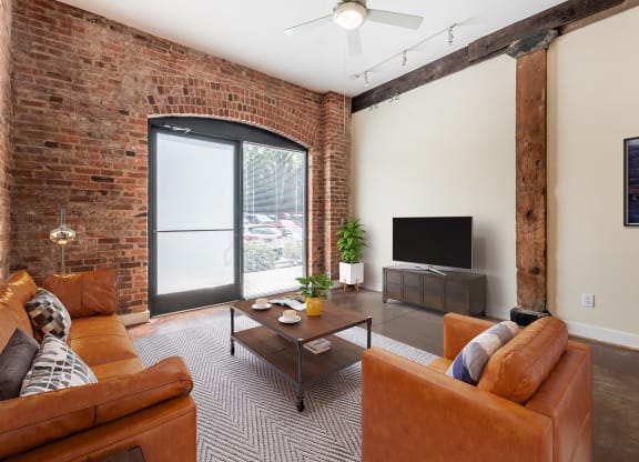 a living room with leather furniture and a brick wall at Mayton Transfer Lofts in Virginia 23803