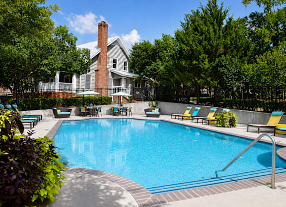 A large swimming pool surrounded by trees and chairs.
