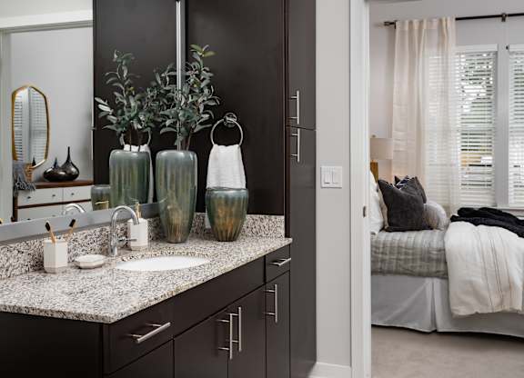 A bathroom with a sink, mirror, and vases on the counter.