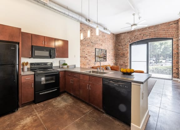 a kitchen with black appliances and wooden cabinets and a brick wall at Mayton Transfer Lofts in VA 23803